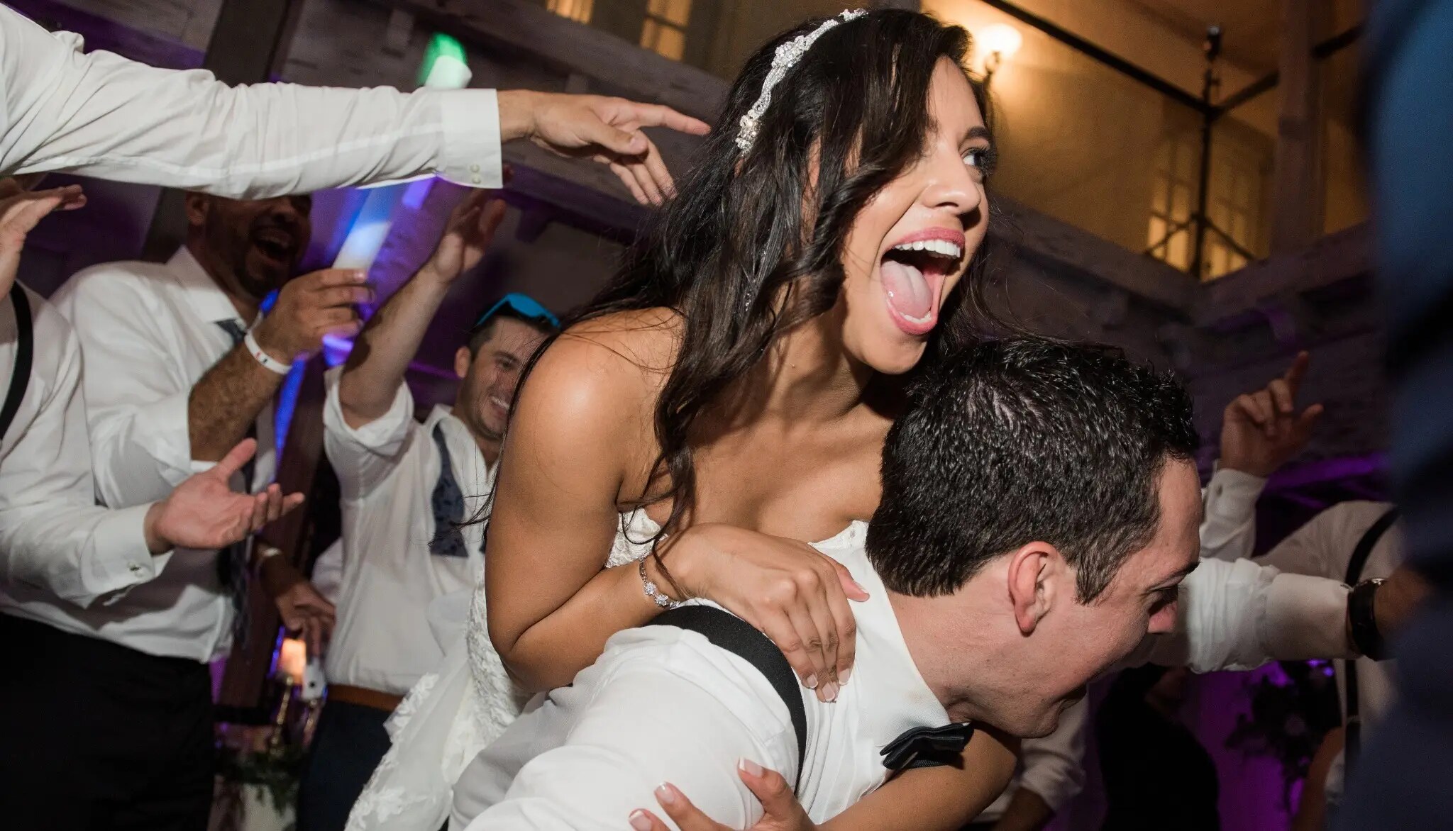 A joyful bride riding on the groom's back in the middle of a packed wedding dance floor